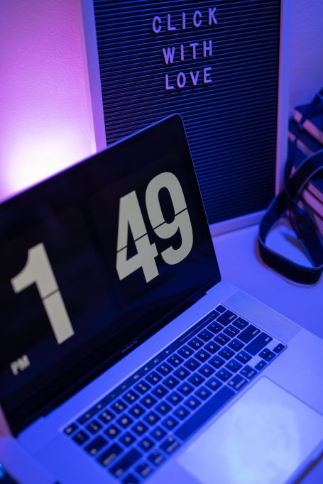 MacBook pro with time on the display. Purple lighting, moody – sign in background says, "click with love".